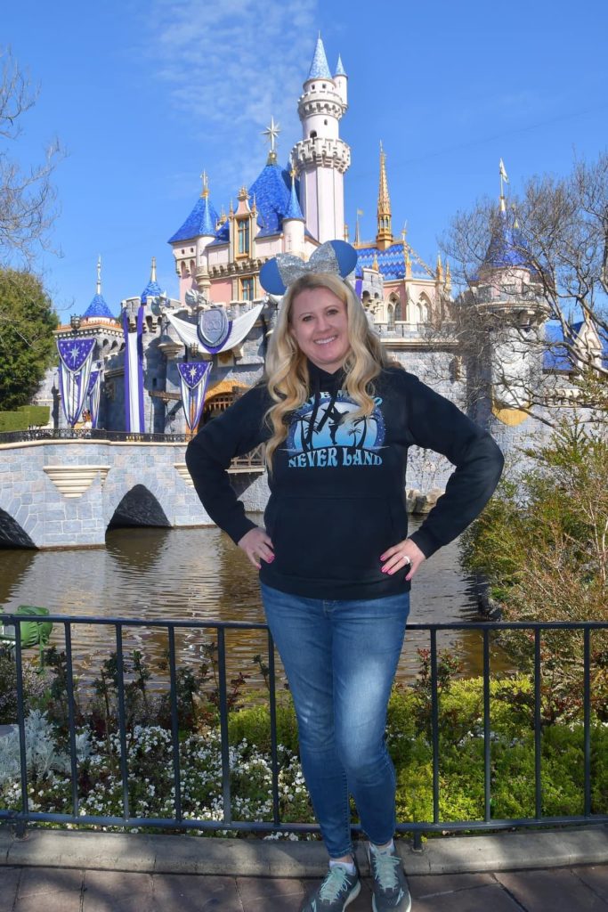 Melissa, author of Mix In Some Magic, standing in front of Cinderella castle smiling.